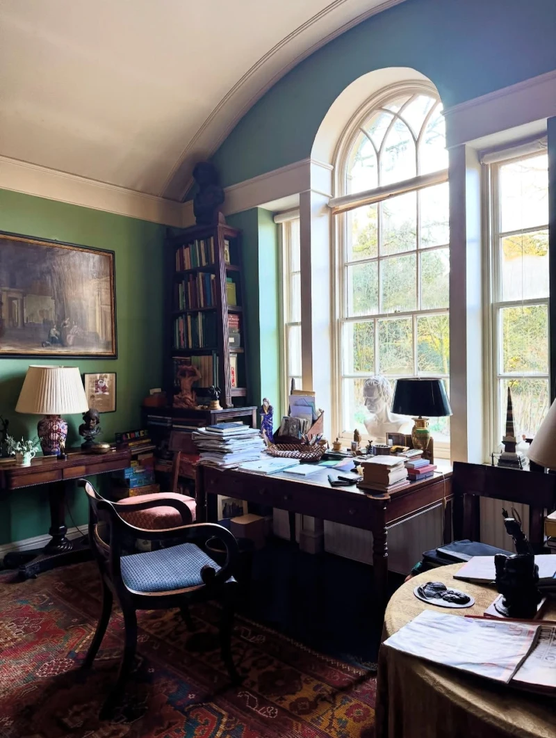 Green Library Study with Arched Window, Antique Desk, and Layered Books