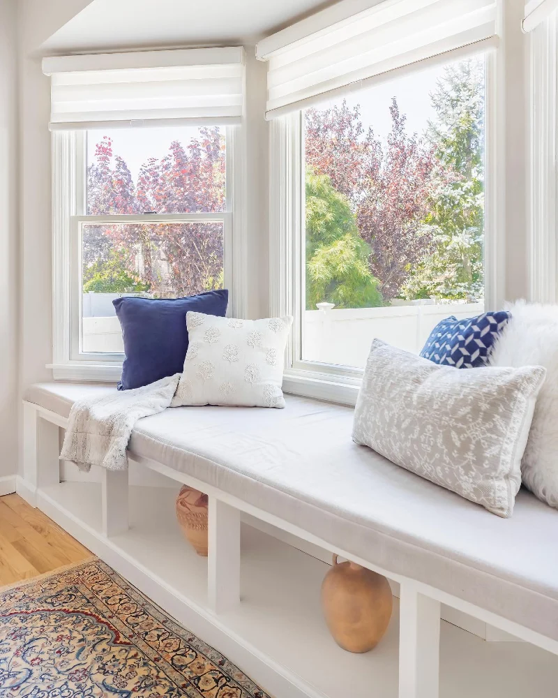 Layered White Roller Shades Above a Bright Window Bench