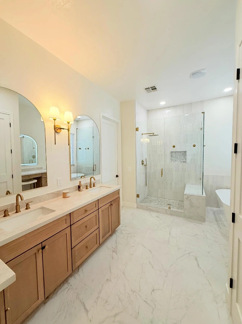 Light Wood Double Vanity with Arched Wall Sconces and Glass Enclosure