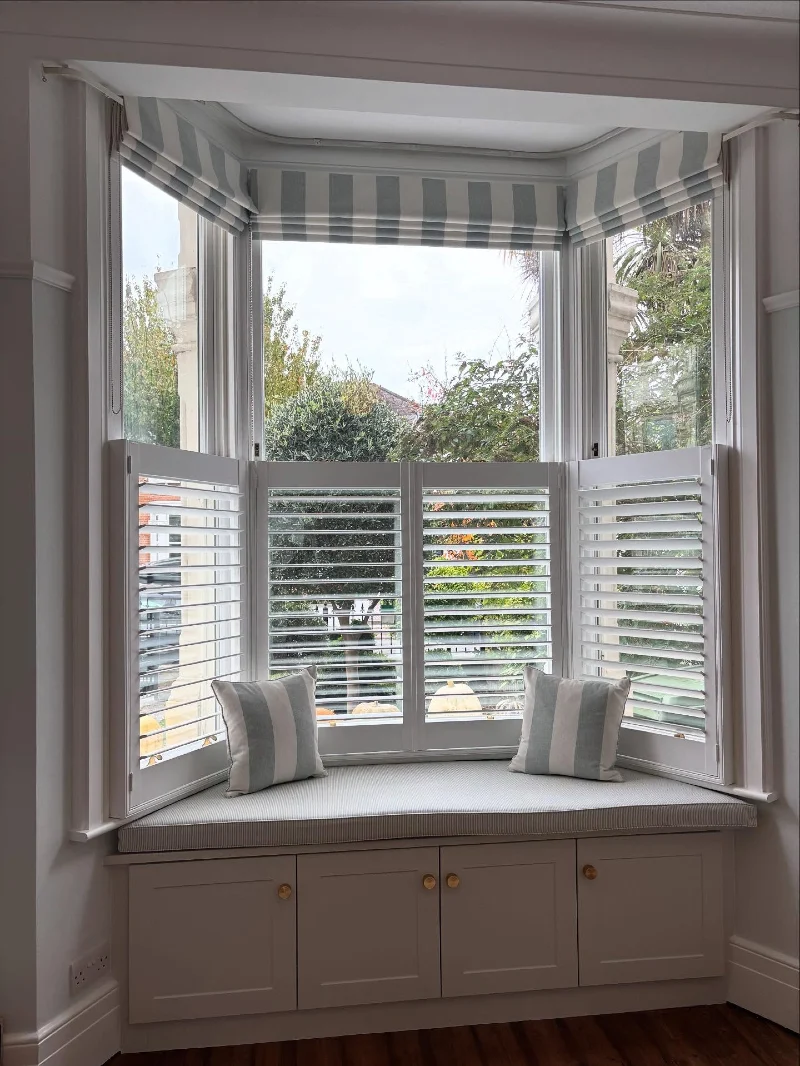Striped Roman Shades Layered Above White Plantation Shutters